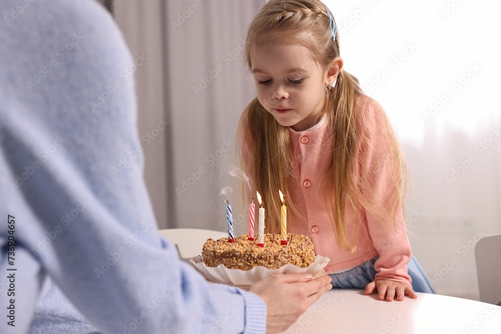 Birthday celebration. Mother holding tasty cake with burning candles near her daughter indoors Birthday celebration. Mother holding tasty cake with burning candles near her daughter indoors