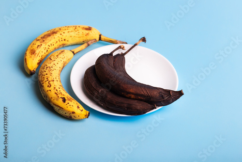 Spoiled yellow and brown bananas on a white plate on a light blue background. Food waste and excessive food consumption in the world. Spoiled fruits.