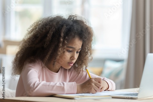 African American little girl with curly hair sitting at the table, writing and doing homework
