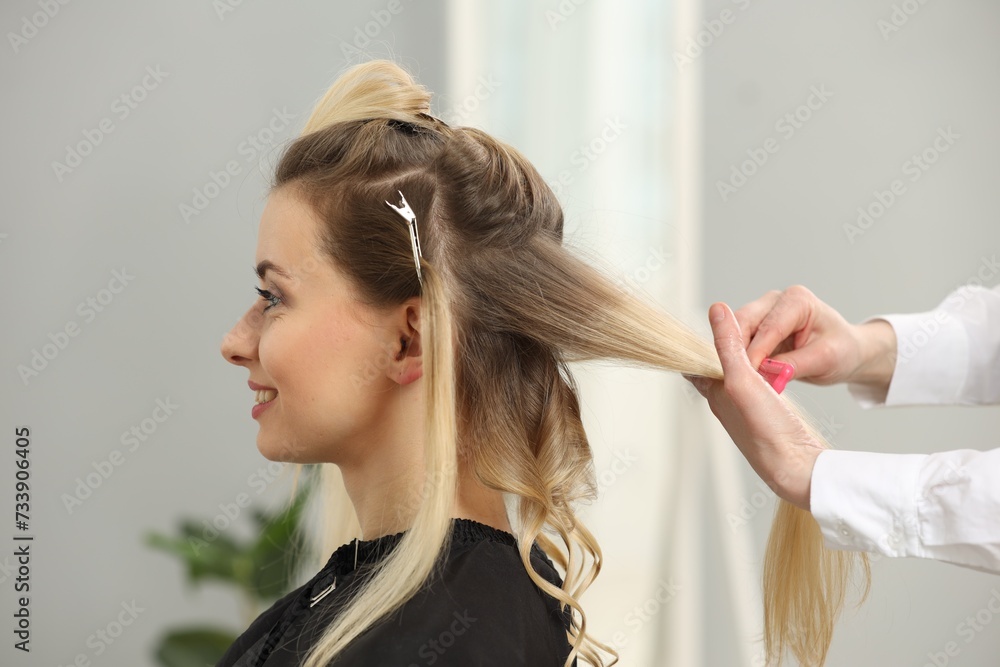 Fototapeta premium Hair styling. Professional hairdresser combing woman's hair indoors, closeup