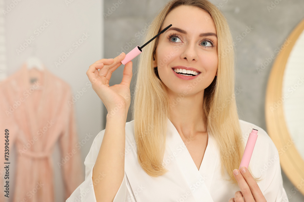 Beautiful happy woman applying mascara in bathroom Beautiful happy woman applying mascara in bathroom