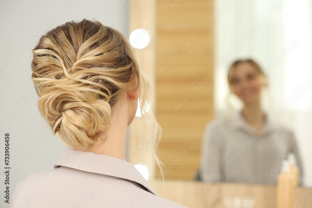 Woman with beautiful hair style looking at mirror indoors. Space for text Woman with beautiful hair style looking at mirror indoors. Space for text