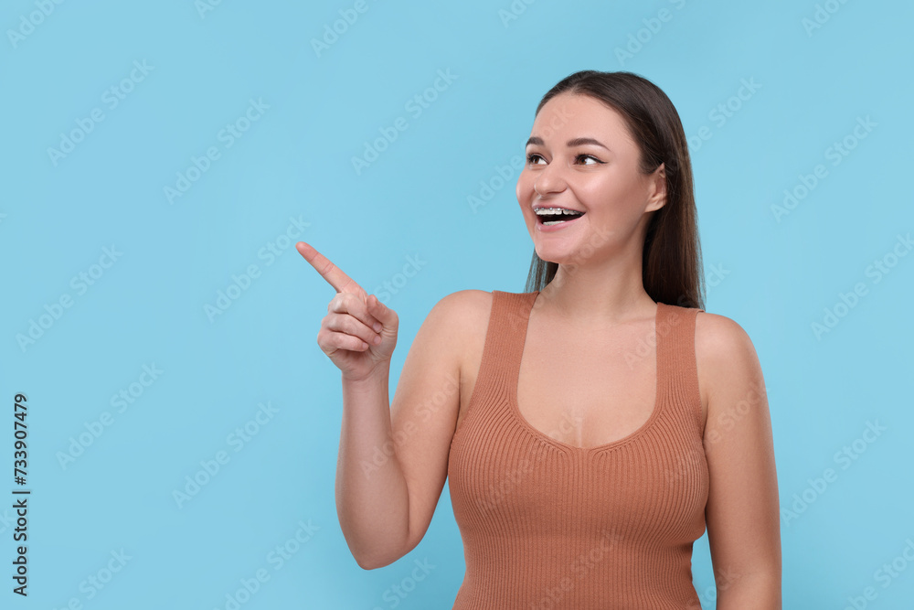 Smiling woman with dental braces pointing at something on light blue background. Space for text Smiling woman with dental braces pointing at something on light blue background. Space for text