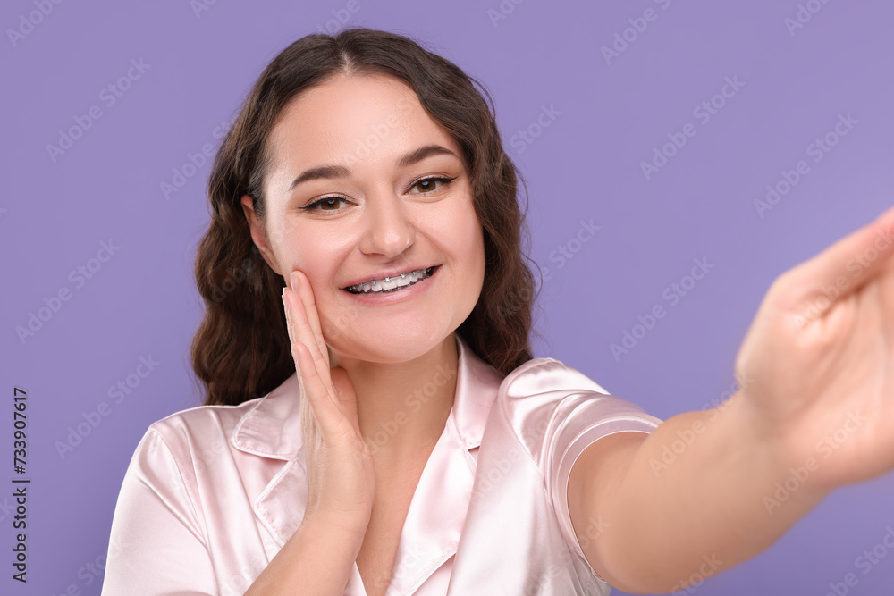 Smiling woman with braces taking selfie on violet background Smiling woman with braces taking selfie on violet background