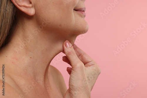 Mature woman touching her neck on pink background, closeup. Space for text