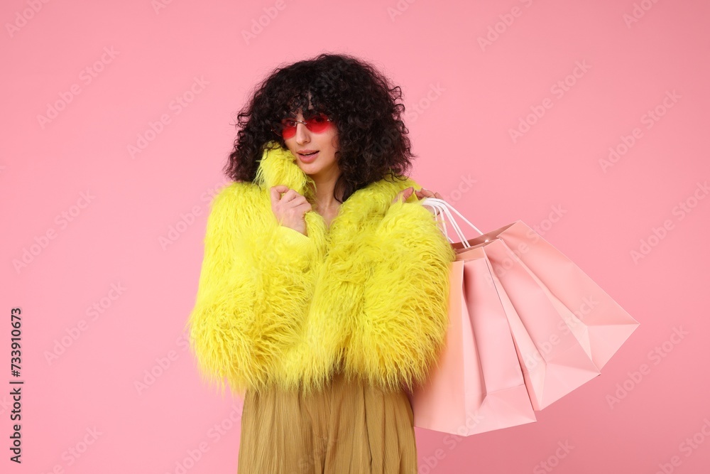 Happy young woman with shopping bags on pink background