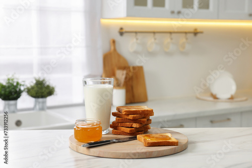 Breakfast served in kitchen. Crunchy toasts, honey and milk on white marble table