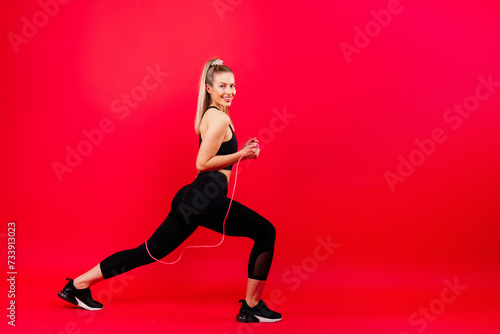 Fitness woman doing jumping exercises with skipping rope on colorful yellow red background.