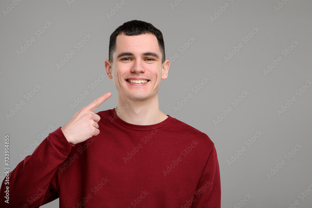 Handsome young man showing his clean teeth on grey background, space for text Handsome young man showing his clean teeth on grey background, space for text