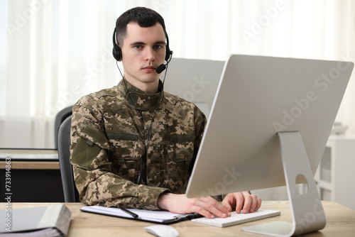 Military service. Young soldier in headphones working with computer at table in office