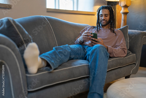 Man with dreads using phone and listening to music while relaxing on sofa