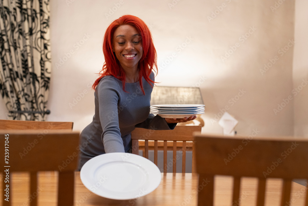 Smiling redhead woman setting table for dinner - obrazy, fototapety, plakaty 