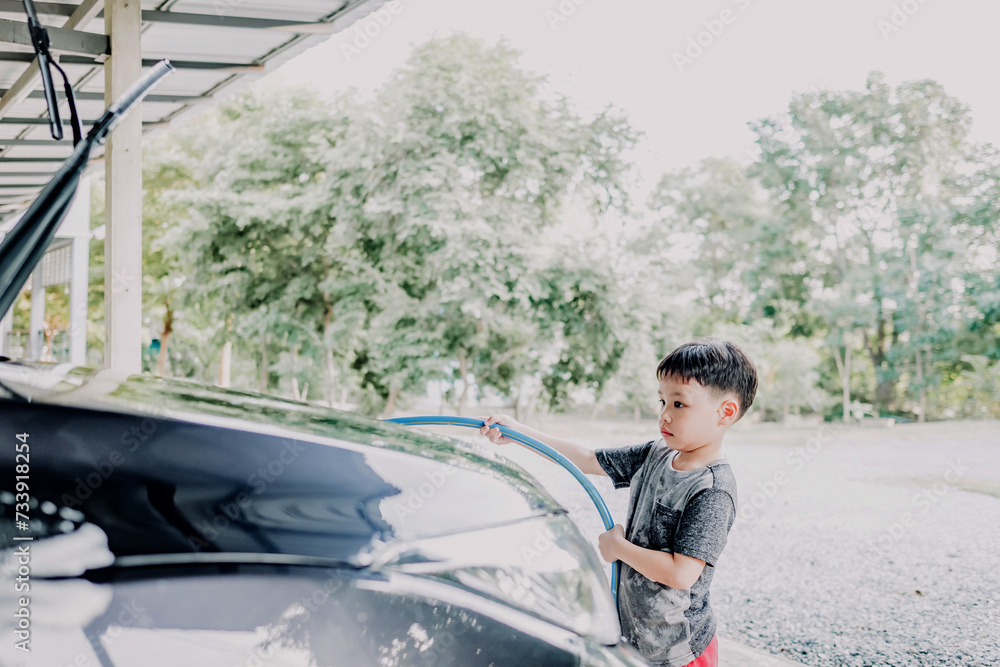 Portrait of little asian boy washing a car on a sunny day. Soft focus. Copy space.