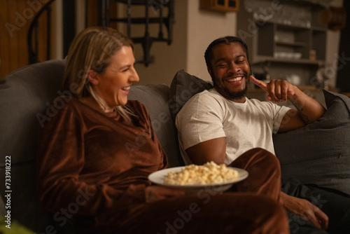 Smiling friends relaxing on sofa at home  sharing popcorn