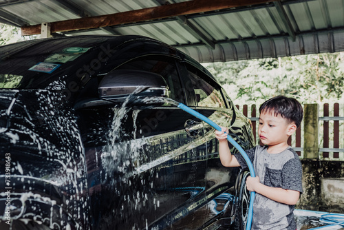 Portrait of little asian boy washing a car on a sunny day. Soft focus. Copy space. © Treechada