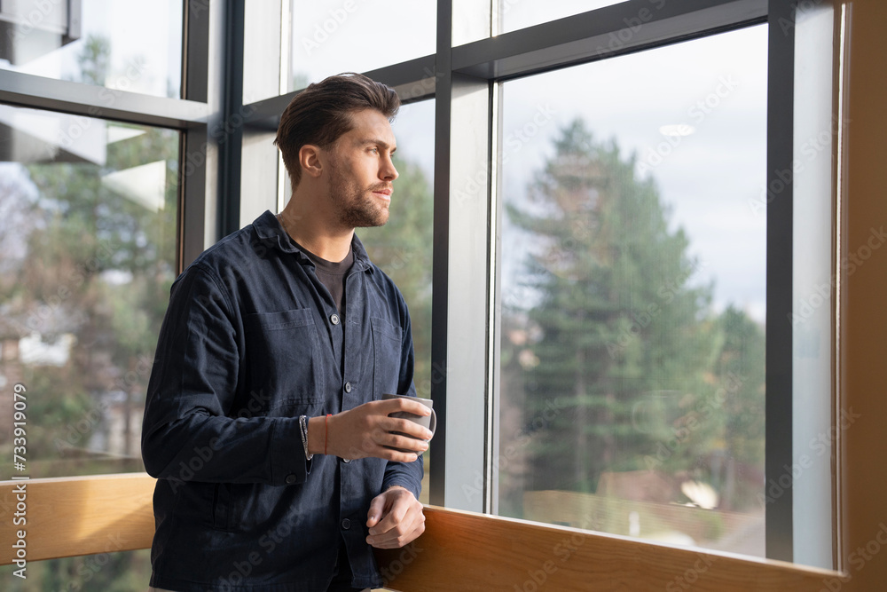 Fototapeta premium Businessman drinking coffee and looking through office window