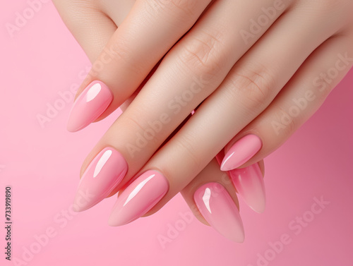 Close-up of a woman's hands with long almond-shaped nails in a glossy pink ombre manicure, set against a pink background