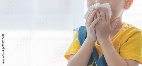 Little boy blowing nose into tissue paper and wearing surgical face mask. Copy space. photo