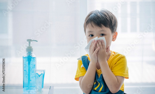 Little boy blowing nose into tissue paper and wearing surgical face mask. Copy space.