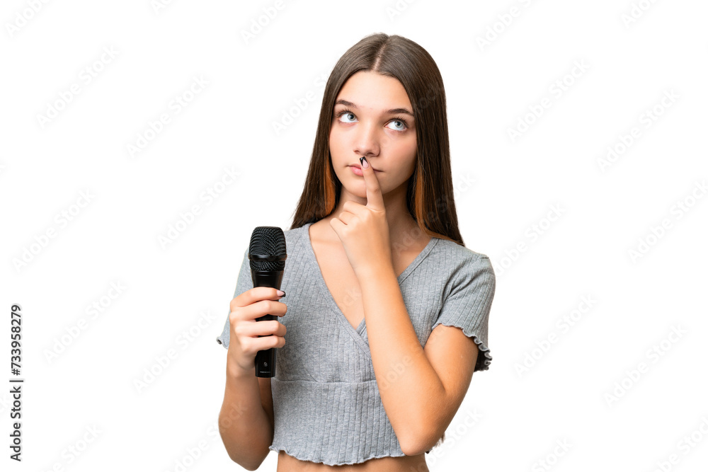 Teenager singer girl picking up a microphone over isolated background having doubts while looking up Teenager singer girl picking up a microphone over isolated background having doubts while looking up