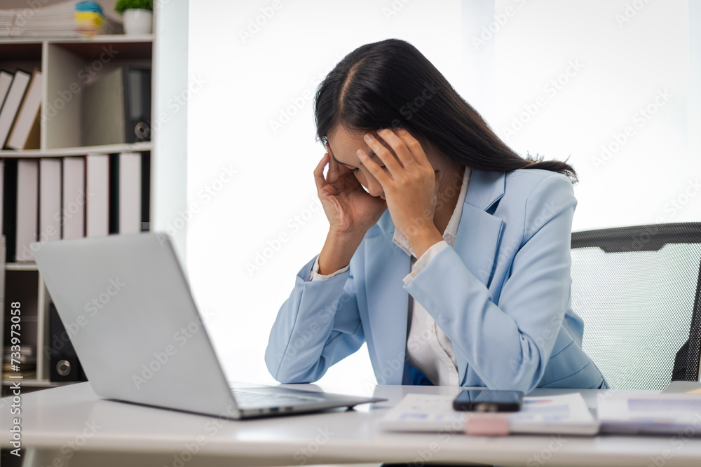 Businesswoman working with laptop in office, she is seriously working, is stressed and tired. Asian woman who is suffering from headache and stress due to overwork. Businesswoman working with laptop in office, she is seriously working, is stressed and tired. Asian woman who is suffering from headache and stress due to overwork.