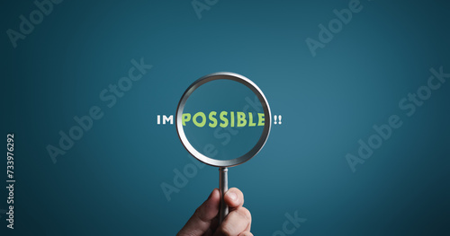 Magnifier focuses on word POSSIBLE side of the word IMPOSSIBLE. It is possible to motivational inspirational concepts. Unveiling the motivation concept. Blue background, flat lay. photo