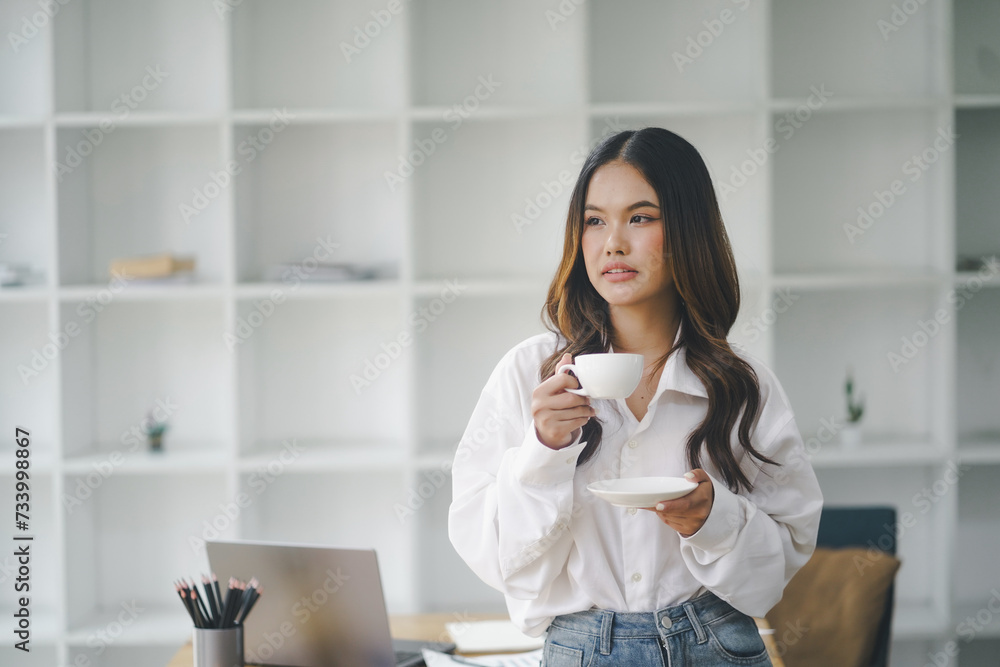 Beautiful young concentrated business woman wearing shirt using laptop while standing in modern workspace Beautiful young concentrated business woman wearing shirt using laptop while standing in modern workspace