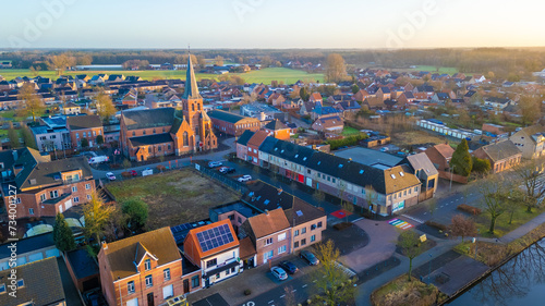 This aerial shot captures the quaint town of Rijkevorsel during the soft light of dusk. The Sint Jozef Church, with its towering spire, stands prominently among the surrounding residential buildings