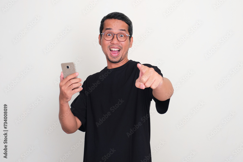 A man pointing at the camera and holding mobile phone with excited expression A man pointing at the camera and holding mobile phone with excited expression