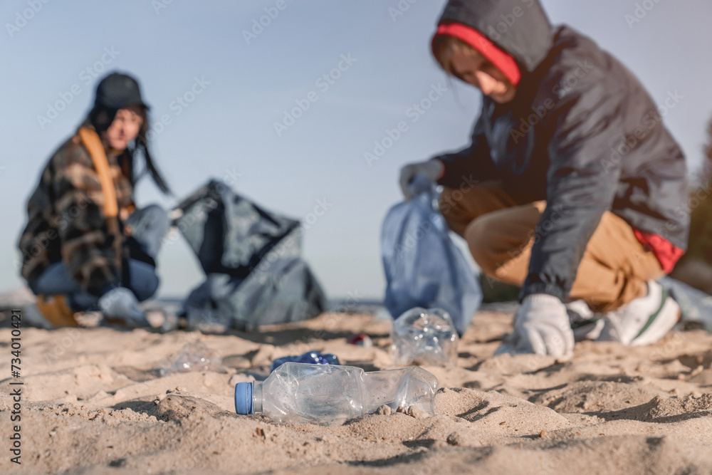 Plastics in the beach with group of volunteers in the background. Focus on plastic on the foreground. Collecting the trash plastic bottles. Pollution contamination of coastline