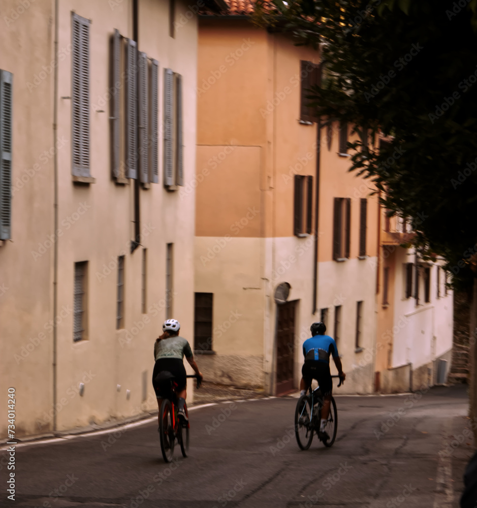 Two cyclists pedal through the streets of Lombardy.