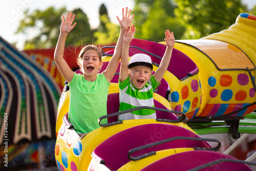 Boy and Girl on a thrilling roller coaster ride at an amusement park with arms raised and yelling with excitement. Summer fun concept photo