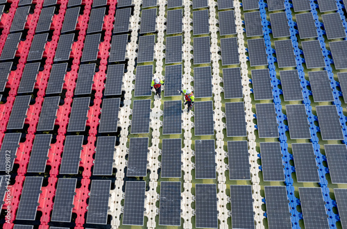 Wide shot of aeroview or top view of two technician workers walk along the solar panel system over water resirvoir for green ecosystem energy for good environment. photo