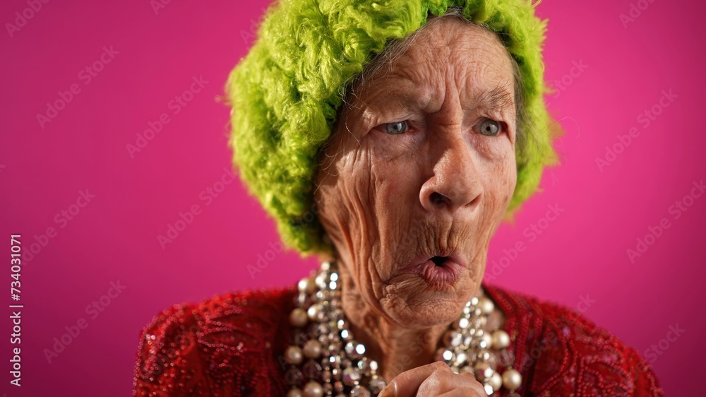 Unhappy displeased fisheye view caricature of funny elderly woman saying NO with green wig or hat isolated on pink background.