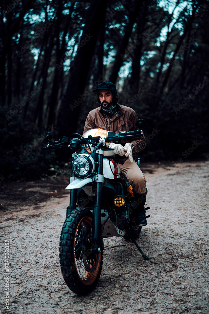 Hombre moreno con moto dentro de un bosque posando y montando por terreno silvestre Hombre moreno con moto dentro de un bosque posando y montando por terreno silvestre