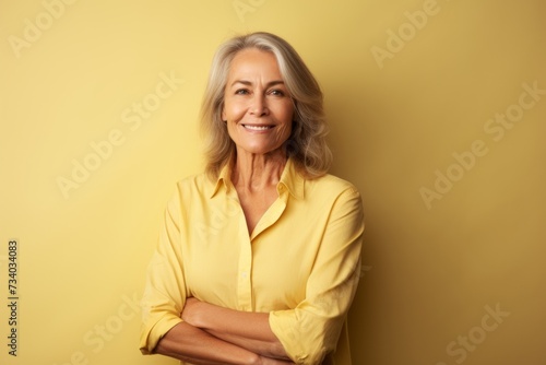 Portrait of happy senior woman with folded arms standing against yellow background © Loli