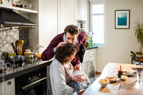 Father kissing mother while she holds a baby in the kitchen photo