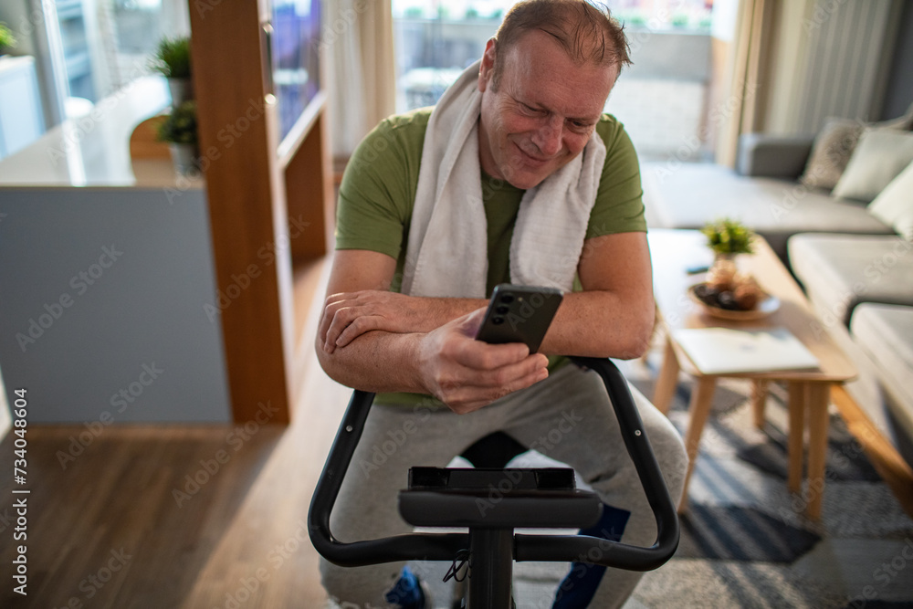 Middle aged man using smartphone on home exercise bike Middle aged man using smartphone on home exercise bike