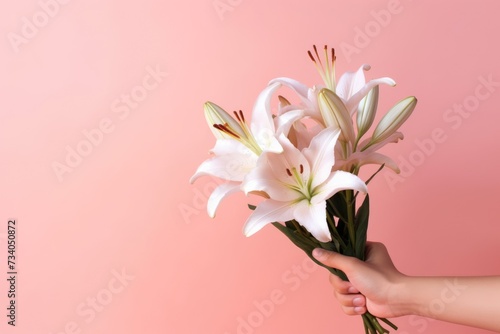 Close up woman s hand holds a bouquet of delicate pink lilies  set against a complementary pink background for a monochromatic effect