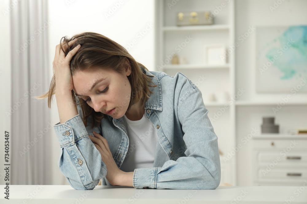 Sad young woman sitting at white table in room Sad young woman sitting at white table in room