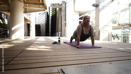 An overweight woman balances on a yoga mat doing pilates stretches with her eyes closed. photo