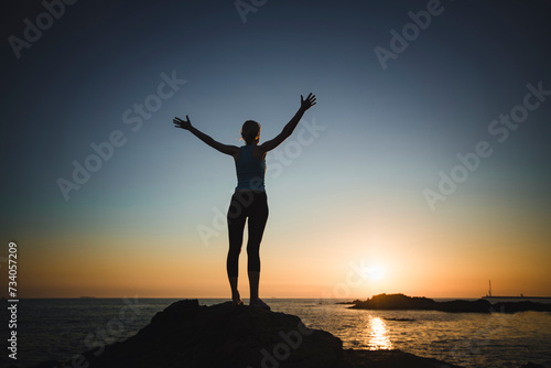 A fit woman meets the sunrise on the ocean shore.
