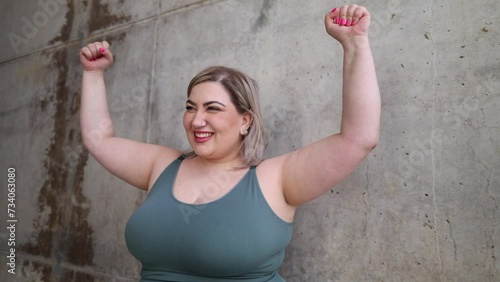Empowered curvy woman posing showing biceps muscles looking at camera, ends up showing middle finger making bad expression, provocation and rude attitude.