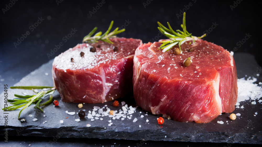 Two fresh raw beef steak mignon with salt, peppercorns and rosemary on dark background