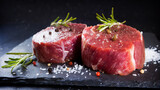 Two fresh raw beef steak mignon with salt, peppercorns and rosemary on dark background