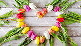 Beautiful spring tulips flat lay in heart shape on rustic wooden planks with copy space for text. Celebrations concept