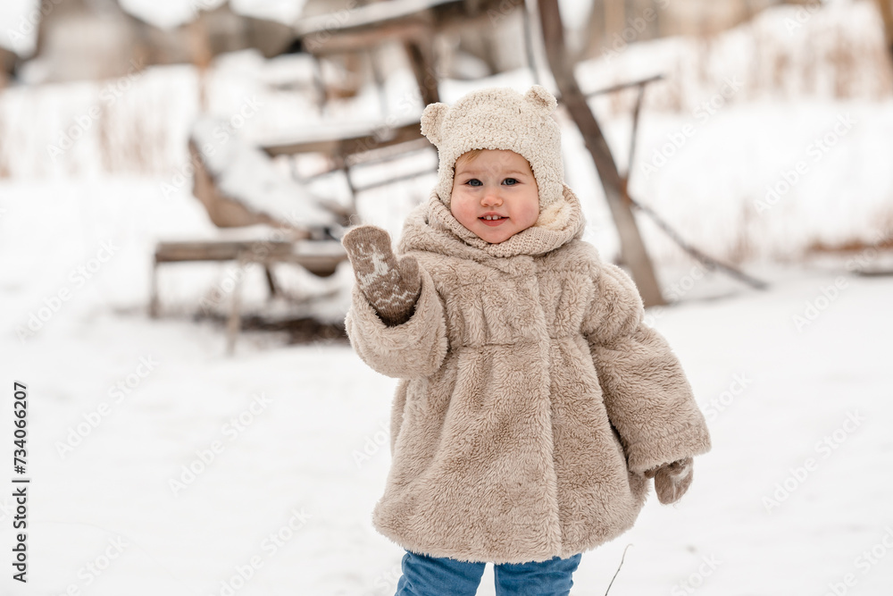 Obraz premium Cute little baby child toddler in a plush hat and fur coat on a snowy winter landscape with reeds. A cozy winter season, an active childhood, the baby looks like a teddy bear