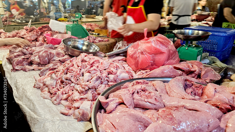A butcher's stall with an array of raw meats on display, including pork and offal, in a busy market