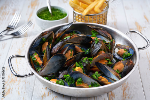 Mussels with french fries and herbs in cooking pan. White background. Close up.