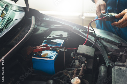 Auto mechanic uses multimeter to check the voltage level in a car battery during a vehicle maintenance procedure..